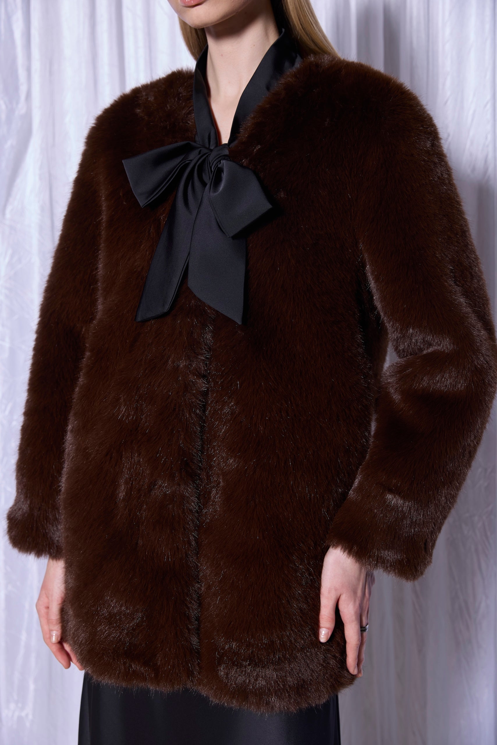 Brown fur coat with a black bow worn by a person against a white background