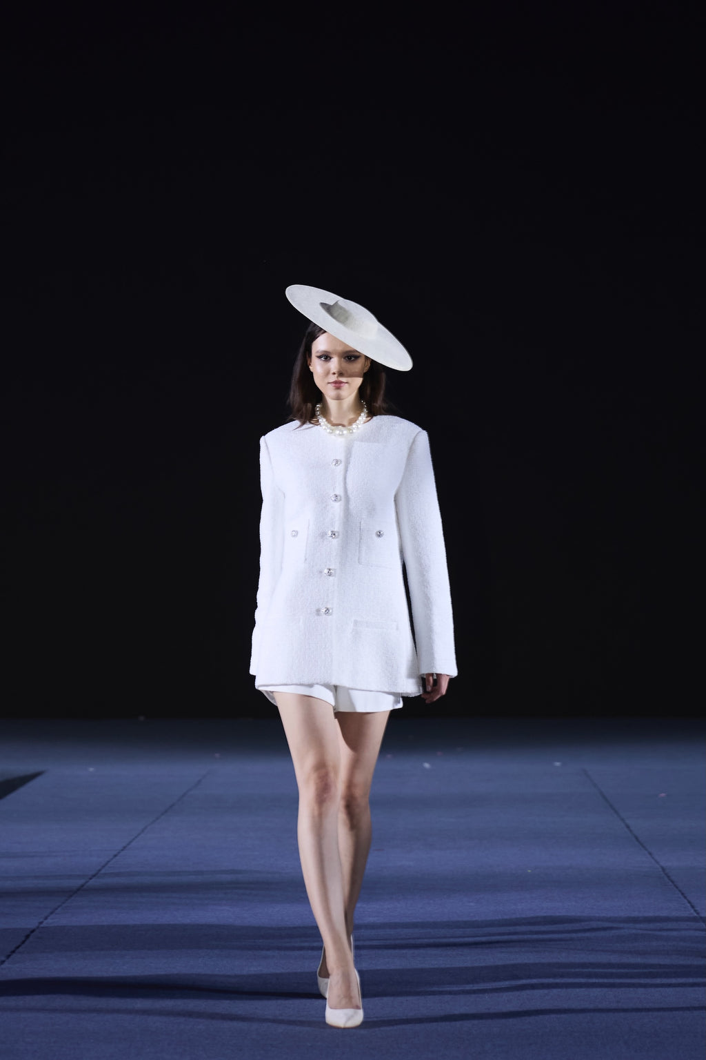 Model wearing a white outfit with a hat on a runway