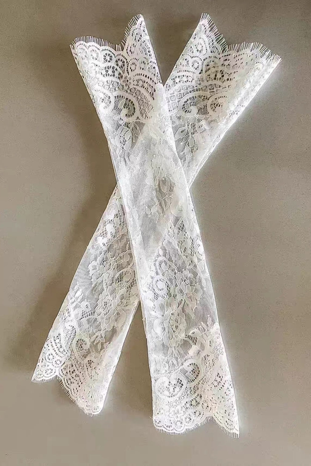 Pair of white lace bridal long gloves on a beige background