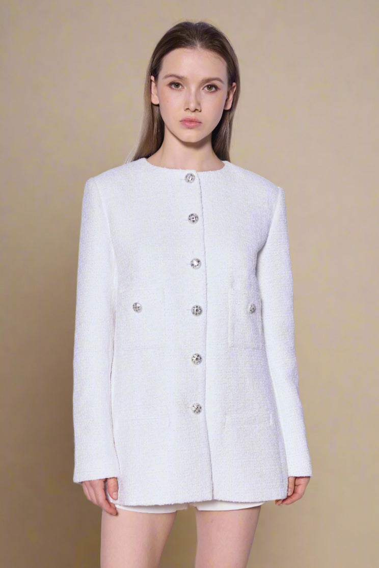 Woman wearing a white jacket with button details against a light background