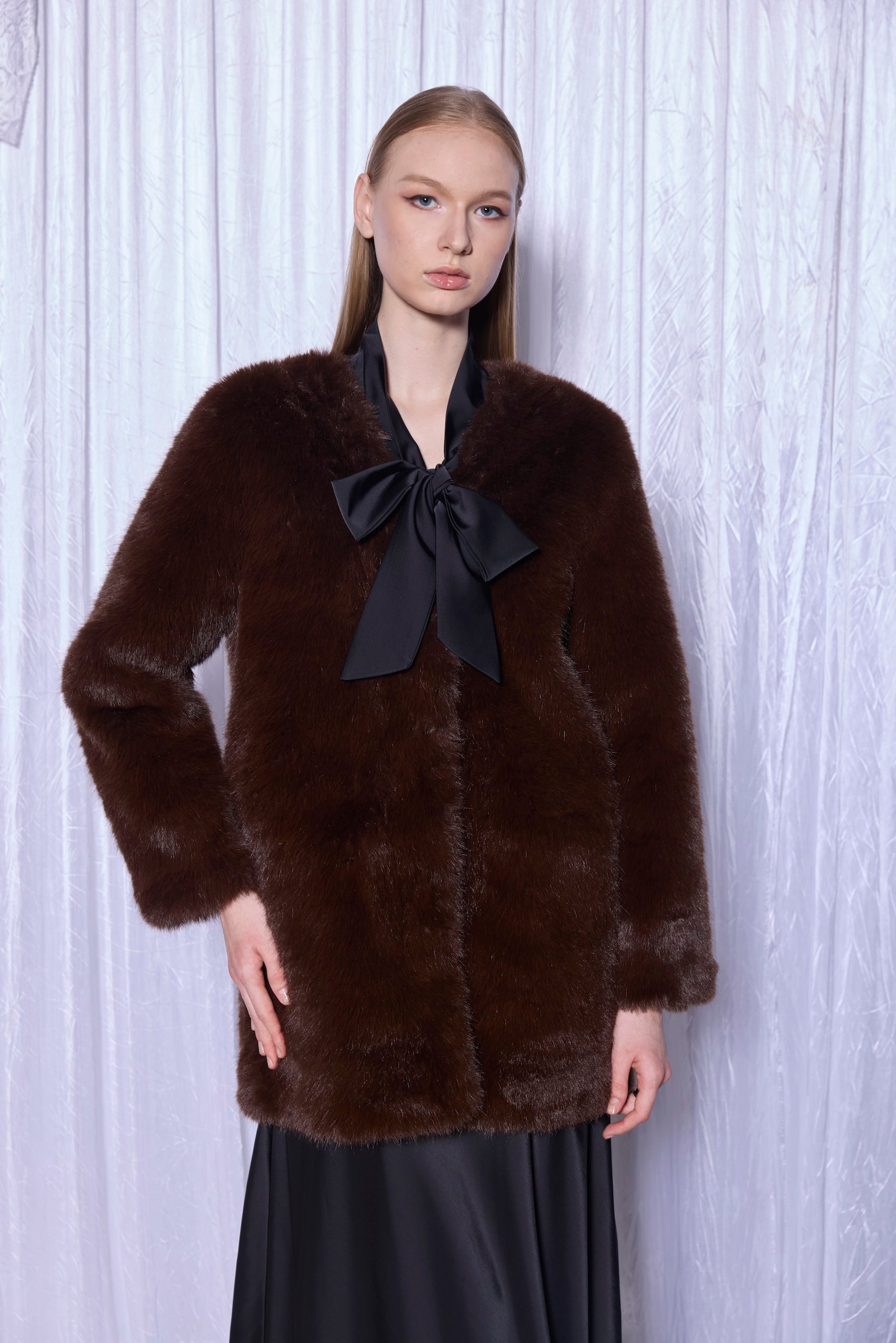 Woman wearing a brown fur coat with a black bow against a white background