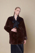 Woman wearing a brown fur coat with a black bow against a white background
