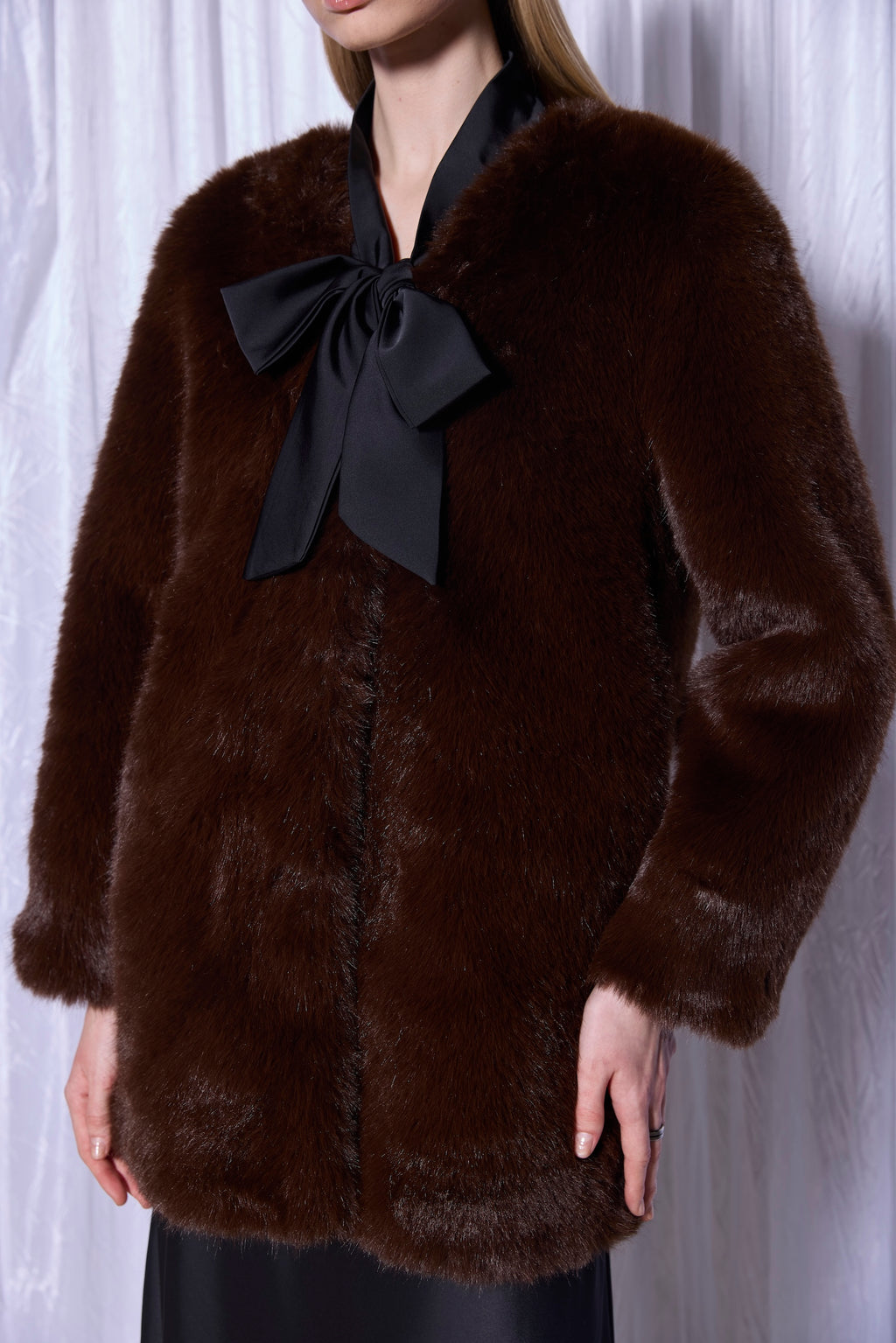 Brown fur coat with a black bow worn by a person against a white background