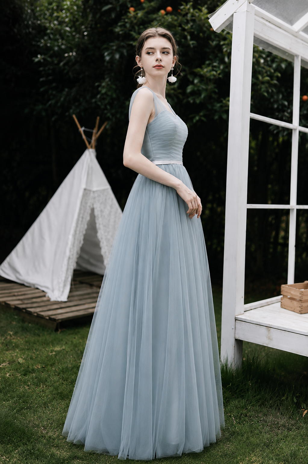 Woman in a light blue dress standing outdoors with a white structure and greenery in the background