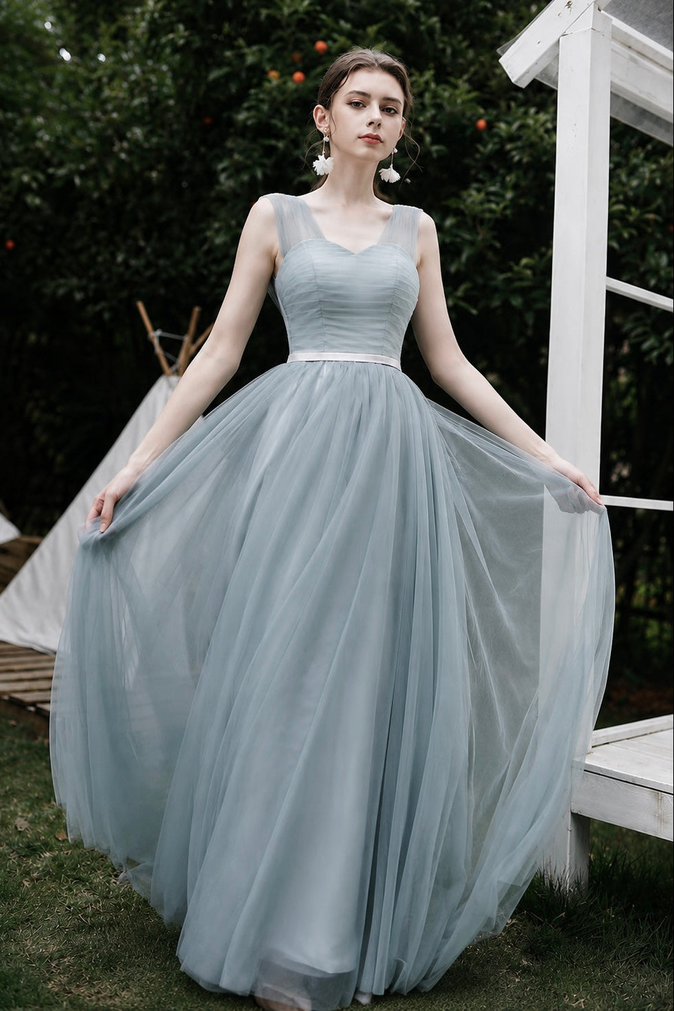 Woman in a light blue dress standing outdoors with greenery in the background