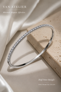 Silver half pavé bangle with zircon stones on a beige stone surface, branded 'Van Atelier'.