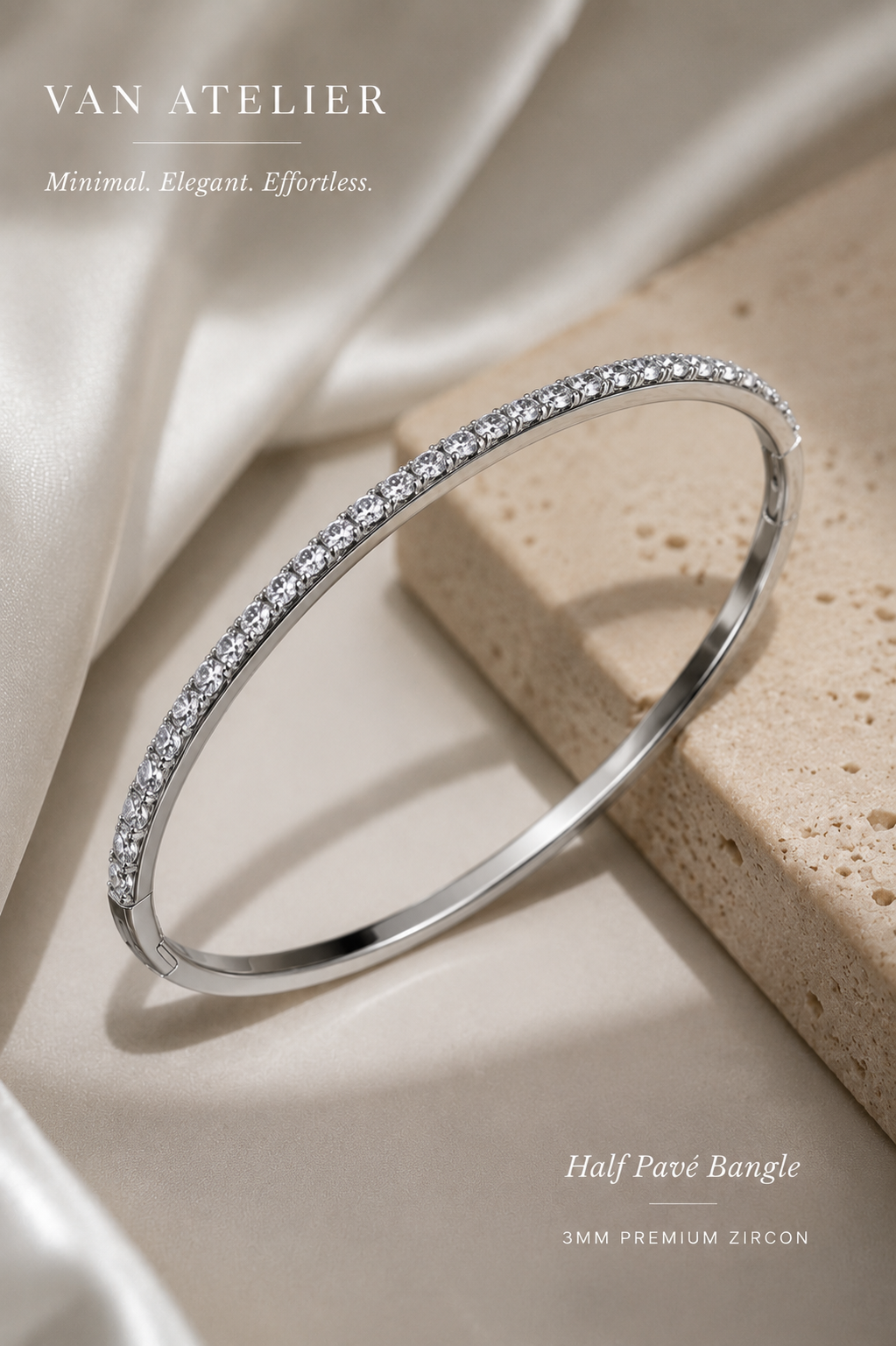 Silver half pavé bangle with zircon stones on a beige stone surface, branded 'Van Atelier'.
