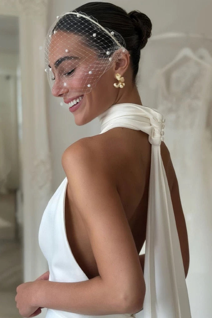Woman in a white wedding dress with a veil and gold earrings, smiling.