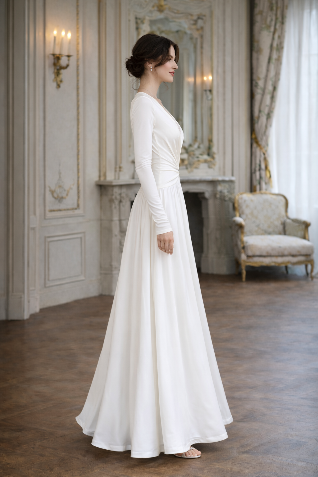 Woman in a white dress standing in an elegant room with a fireplace and chair.