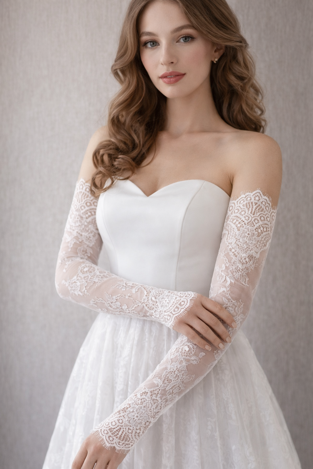 Woman wearing a white strapless wedding dress with lace glove sleeves against a neutral background