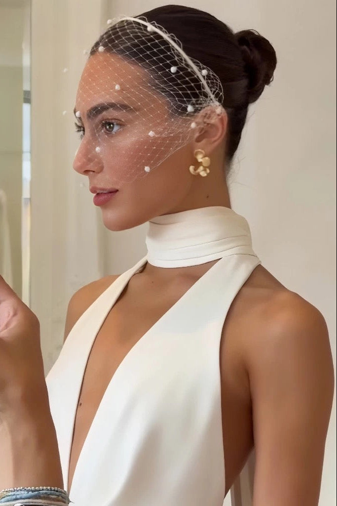 Woman in a white dress with a birdcage veil, holding a phone.