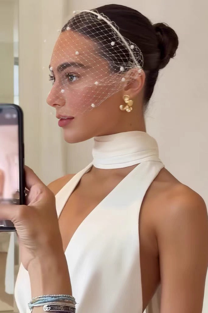 Woman in a white dress with a birdcage veil holding a phone.